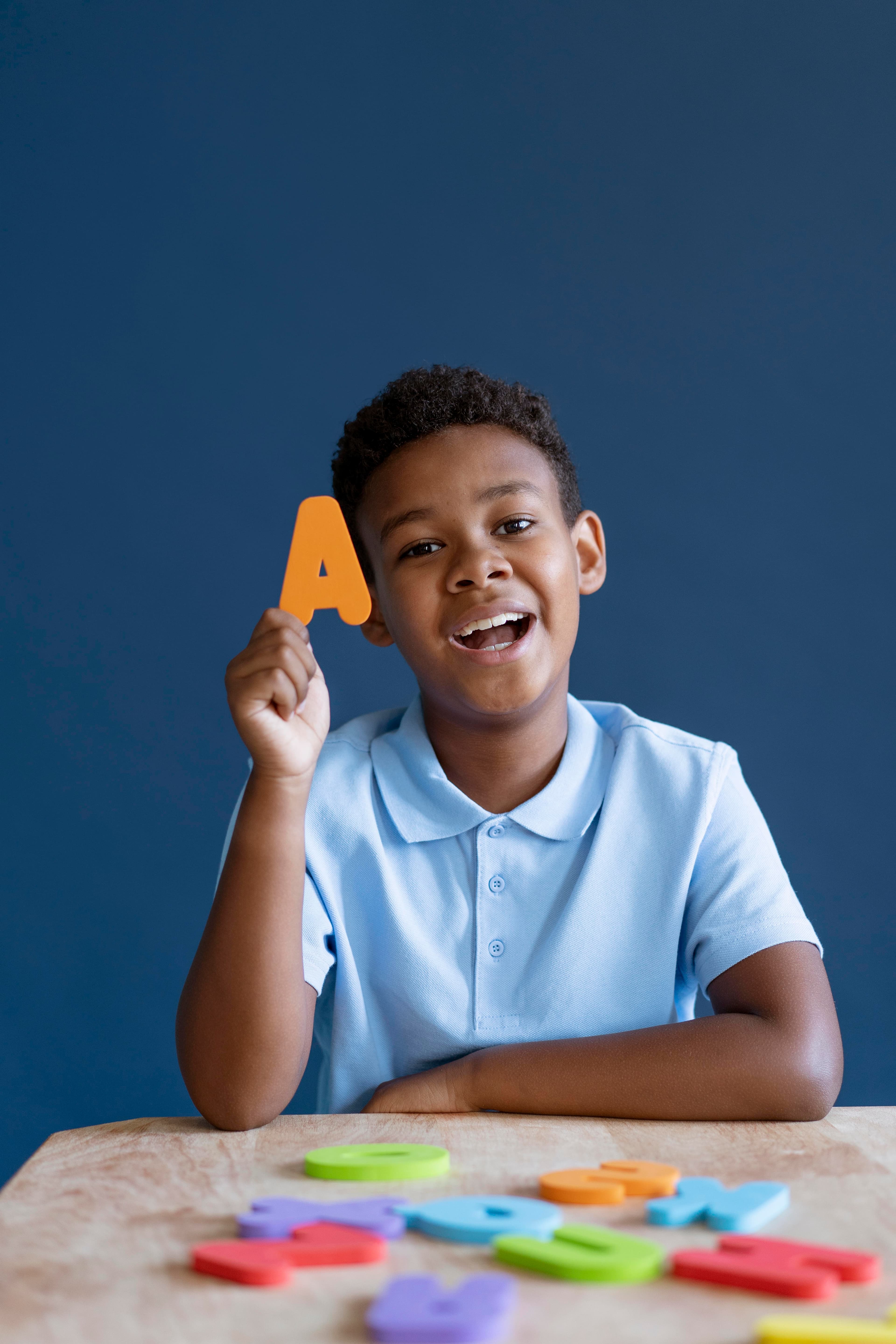Menino sorrindo mostrando uma figura da letra A.